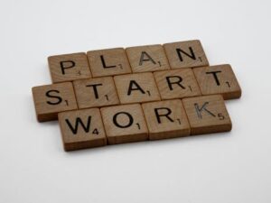 Wooden Scrabble tiles spelling 'Plan', 'Start', 'Work' on a white background.