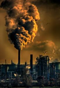 A factory emitting smoke clouds against a dark sunset sky, illustrating air pollution and industrial impact.